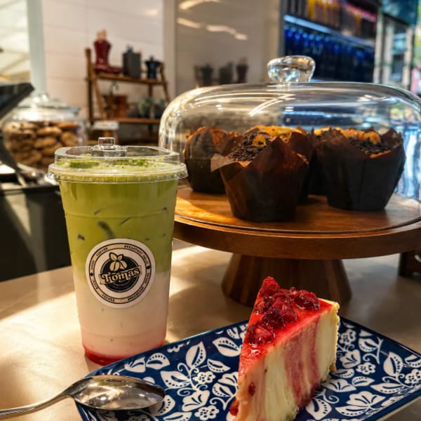 A matcha latte, raspberry cheesecake slice, and chocolate muffins on a cafe counter.