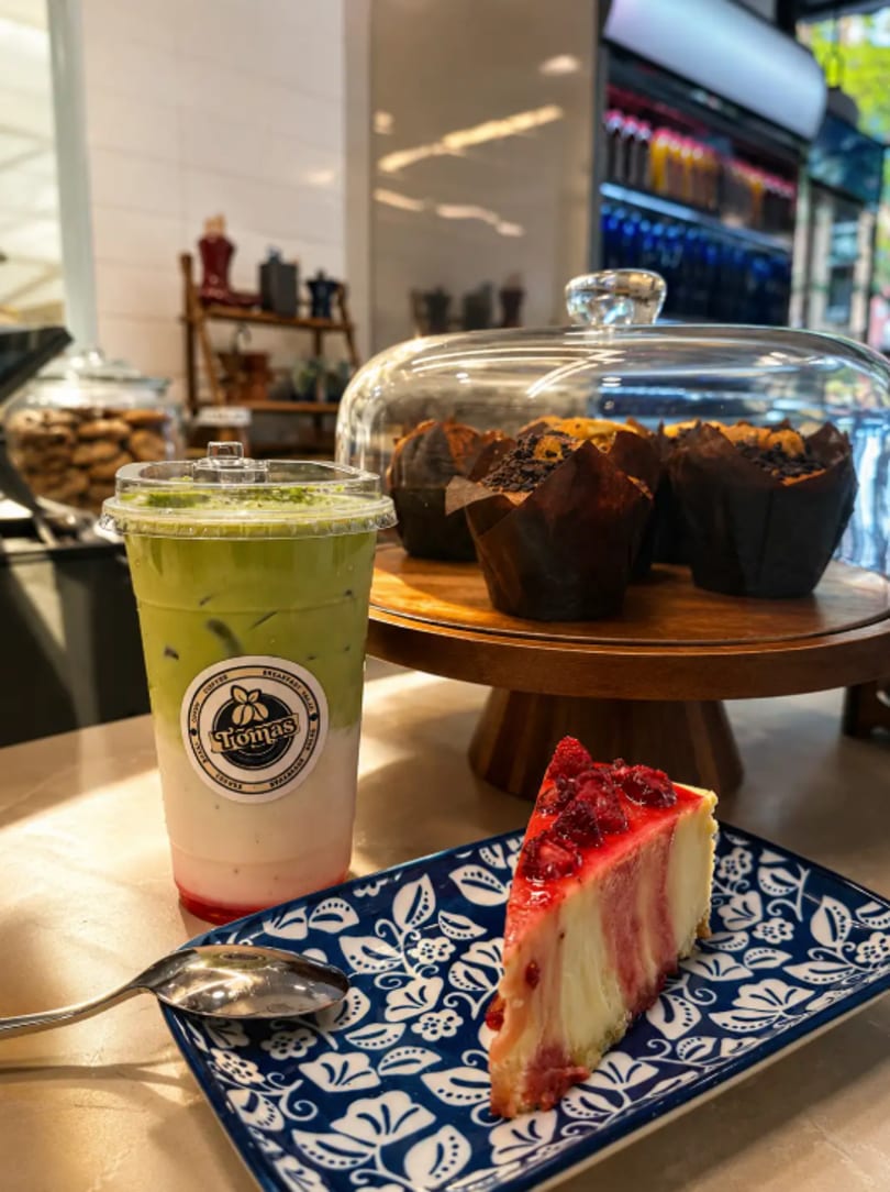 A matcha latte, raspberry cheesecake slice, and chocolate muffins on a cafe counter.
