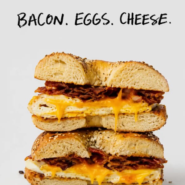 Two halves of a sesame bagel sandwich stacked, filled with crispy bacon, melted cheese, and eggs.