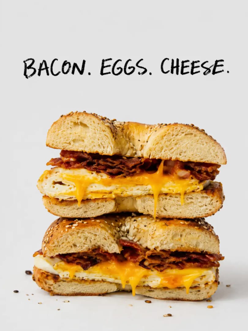 Two halves of a sesame bagel sandwich stacked, filled with crispy bacon, melted cheese, and eggs.